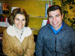 senhora com casaco beje e senhor sentados e a sorrir