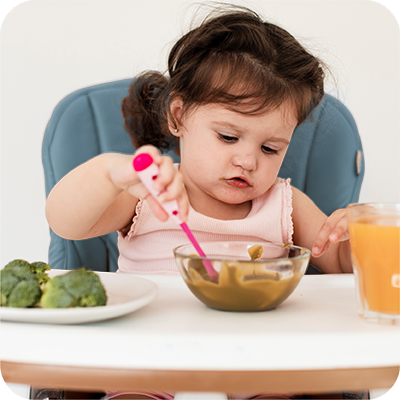 menina  sentada na cadeirinha a comer a papa sozinha