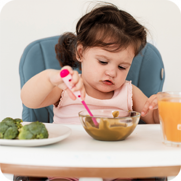 menina  sentada na cadeirinha a comer a papa sozinha